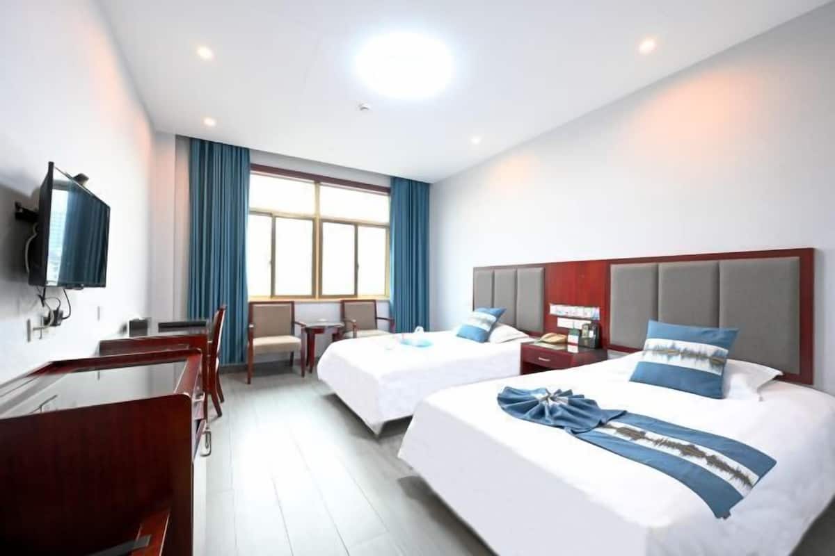 Habitación de hotel con dos camas, un escritorio, una silla, un televisor y un ventanal con cortinas.