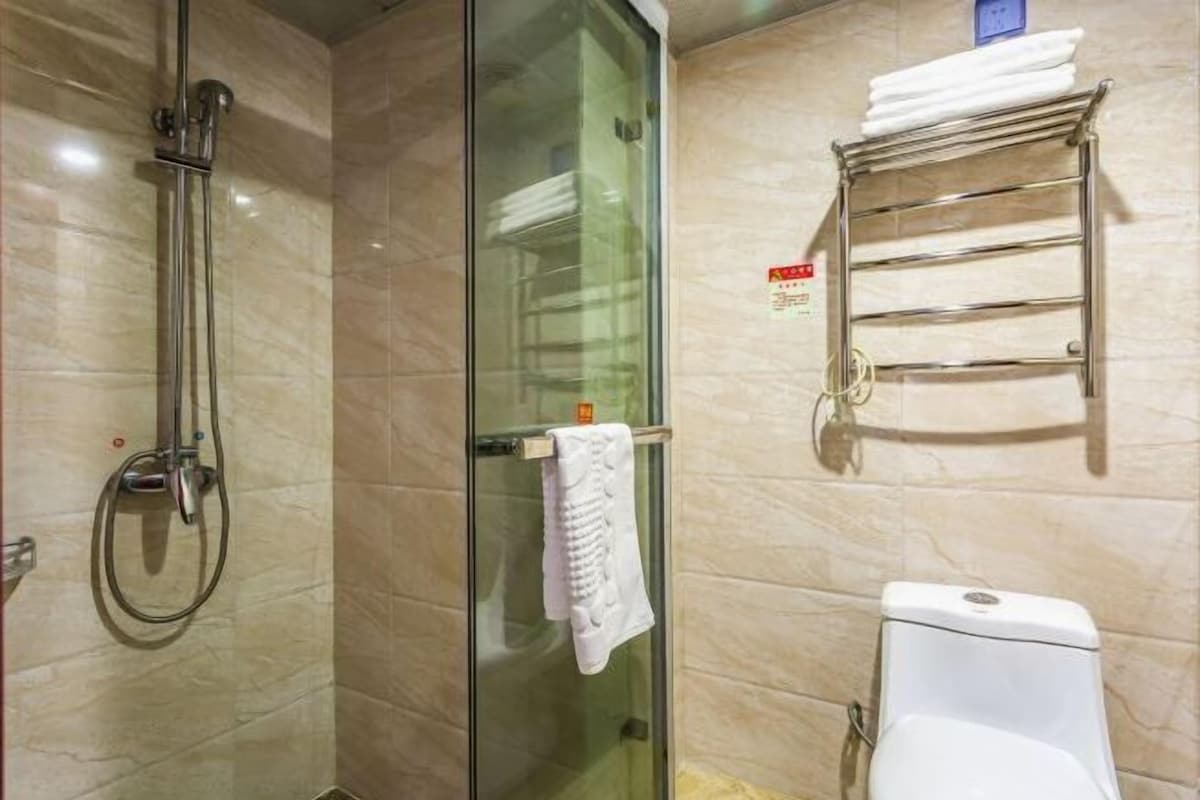 A bathroom with a glass-enclosed shower, a white toilet, and a towel rack with folded towels.