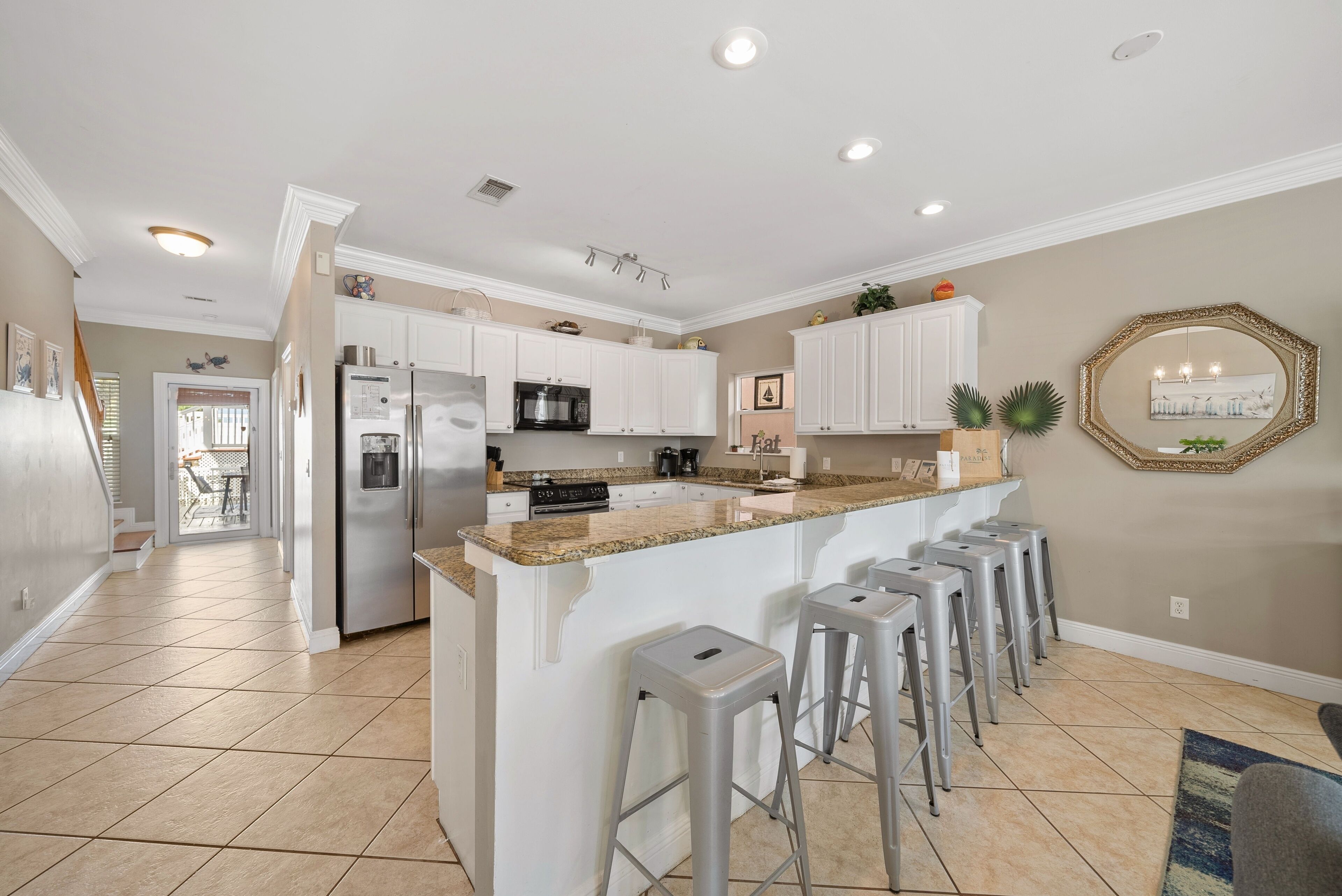 A modern kitchen with white cabinets, a granite countertop, and stainless steel appliances. There are bar stools and a large island with a sink.