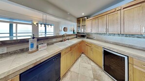 A modern kitchen with wooden cabinets, a dishwasher, a microwave, and a large window providing a view.