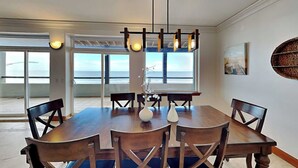 A dining room with a large wooden table, six chairs, and a hanging light fixture.