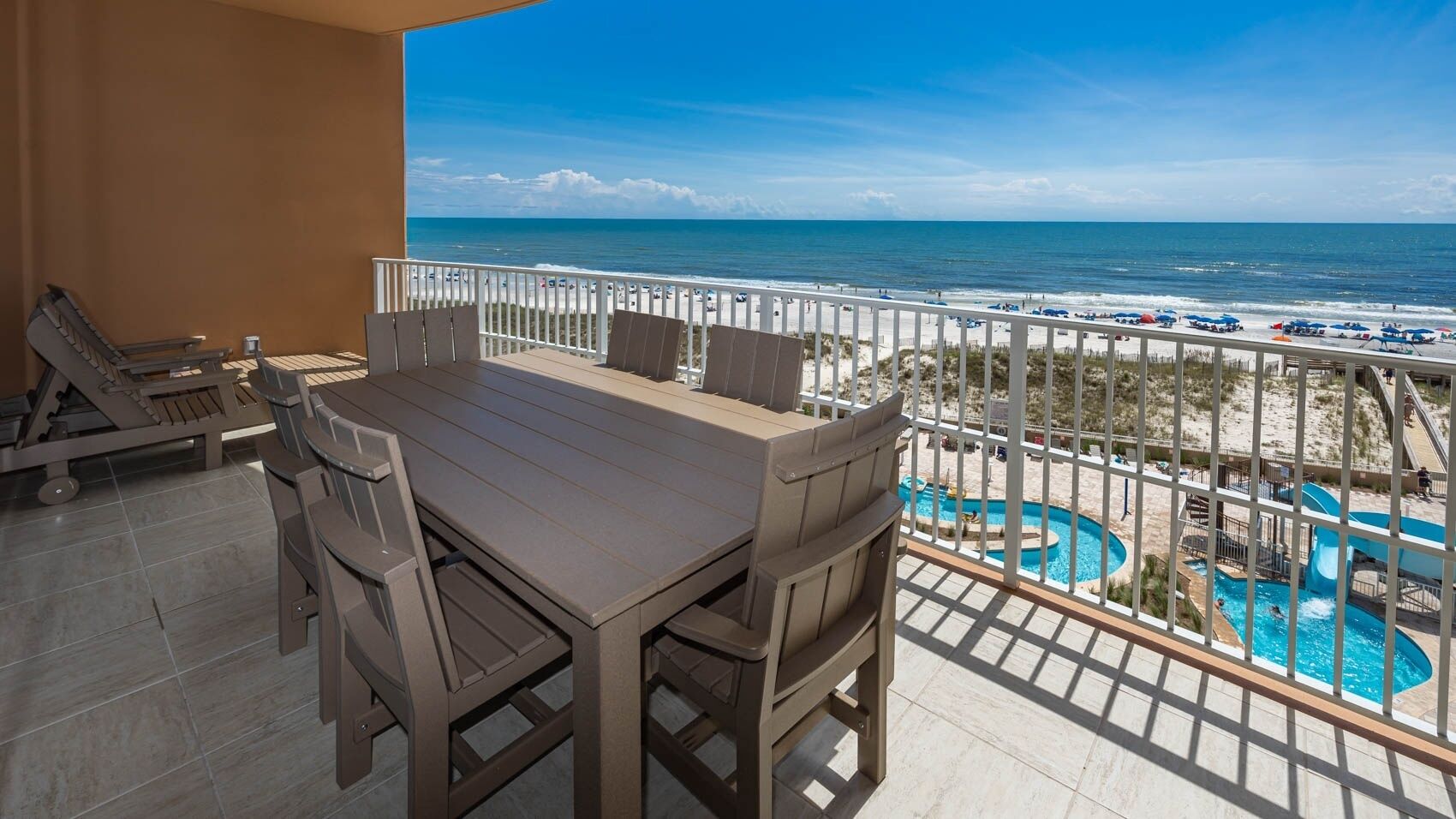 Un balcón con mesa y sillas, con vista a una playa y un área de piscina.