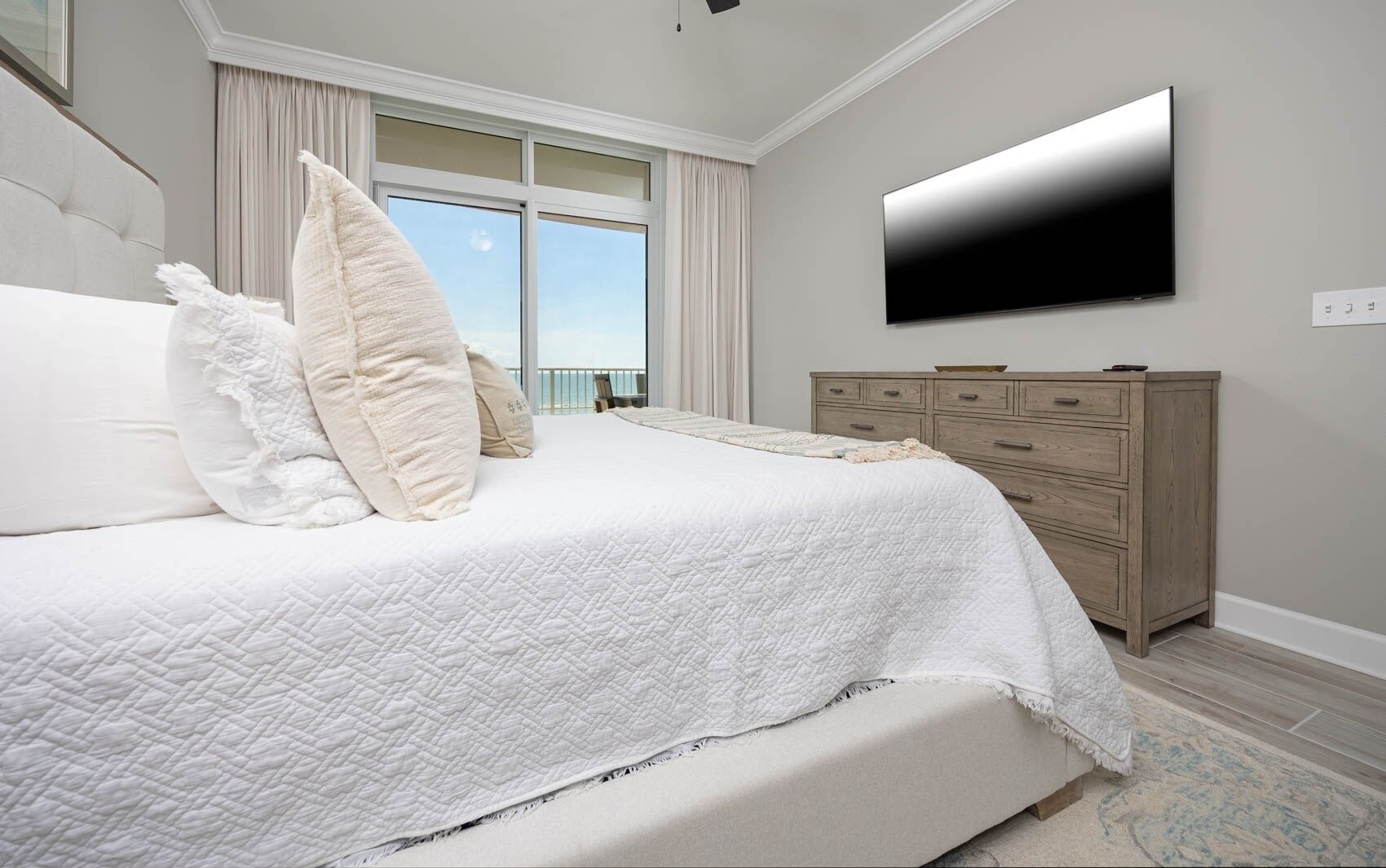 A modern bedroom with a large bed, a flat-screen TV mounted on the wall, and a wooden dresser.