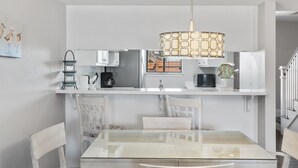 A modern kitchen with white cabinets, a glass dining table, and a hanging light fixture.
