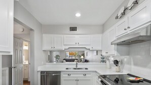 A modern kitchen with white cabinetry, a stainless steel dishwasher, and a black stove.
