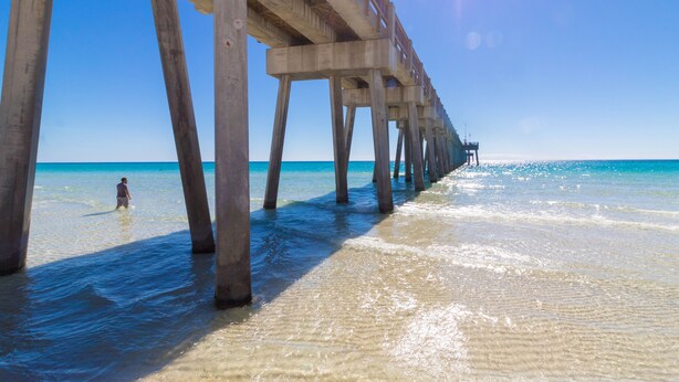 A pier extending into the ocean with clear water and a person standing at the end.