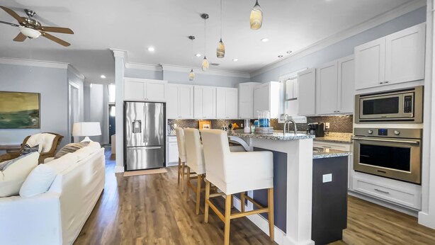 A modern kitchen with white cabinetry, a stainless steel refrigerator, a double oven, and a central island with bar stools.