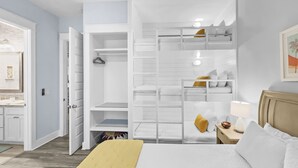 A bedroom with a bunk bed, a bedside table with a lamp, and a wardrobe with open doors.