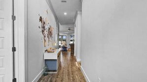 A hallway with wooden flooring, white walls, and a door on the left.