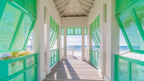 Un paseo cubierto de madera con contraventanas verdes que conduce a una playa.