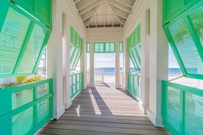 A covered wooden walkway with green shutters, leading to a beach. - Sea La Vie 1 Bedroom Condo by RedAwning (Panama City Beach)