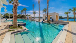 Una piscina azul cristalina rodeada de palmeras y un edificio blanco con techo de vidrio.