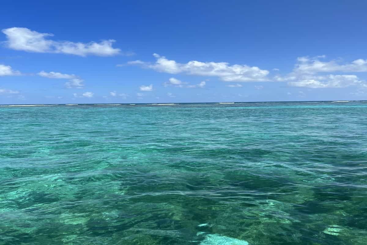 On peut admirer une vue dégagée sur l'eau turquoise de l'océan, avec une côte lointaine sous un ciel bleu parsemé de quelques nuages.