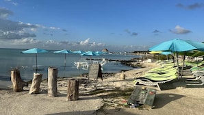 Une plage avec des poteaux en bois, des parasols bleus et des chaises longues.