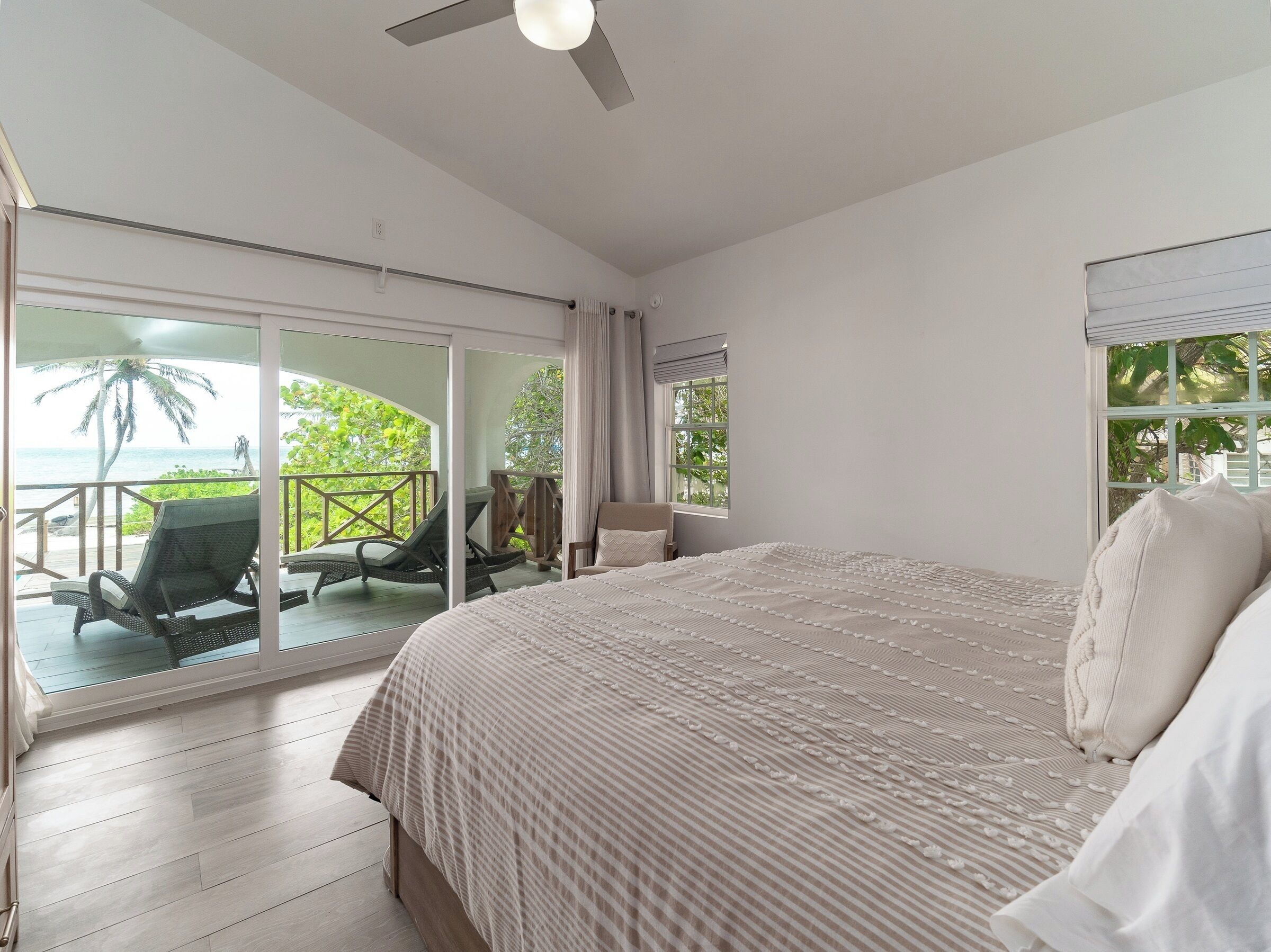 A bedroom with a large bed, a balcony with chairs, and a view of the ocean.