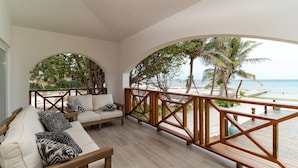 Un balcon avec une balustrade en bois, un canapé agrémenté de coussins à motifs et une vue sur la plage et les palmiers.