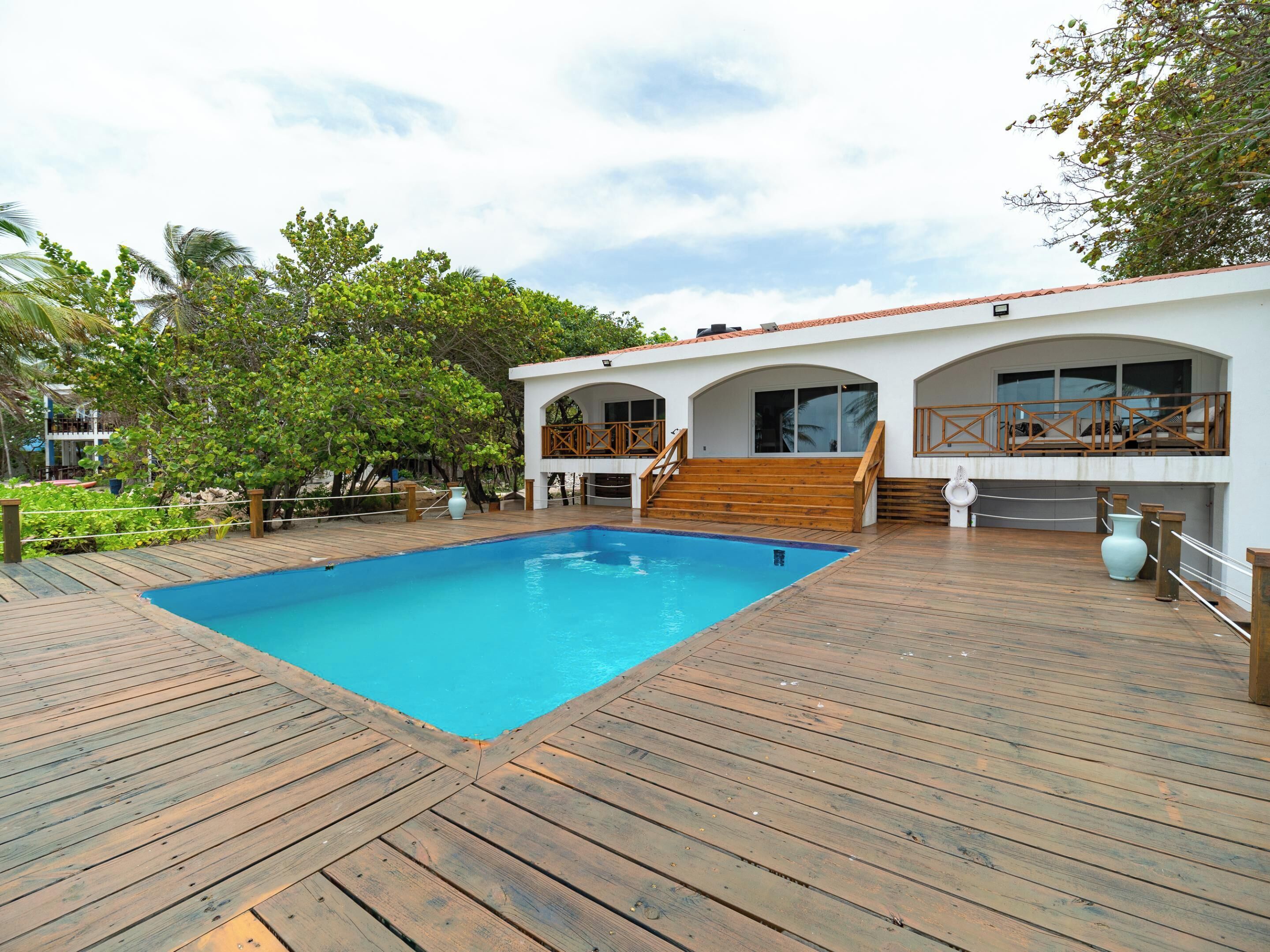 Zona de piscina con cubierta de madera, un edificio blanco con ventanas de arco y un balcón con barandilla de madera.
