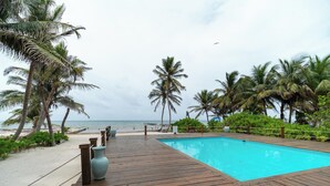 Une terrasse en bois qui mène à une piscine, offrant une vue sur la plage et l’océan.