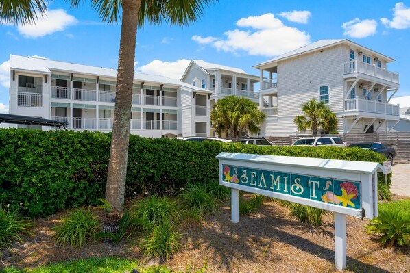 A beachfront hotel with multiple balconies, a signboard with 'SEAMIST' written on it, and lush greenery. - Gulf-Front Getaway — Seamist #5 with Bikes & Spectacular Balcony Views (Seacrest)