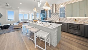 A modern kitchen with a central island, bar stools, and pendant lighting. - "Wait and Sea" New Beachfront Home in PCB with Private Pool and Beach Access! (Panama City Beach)