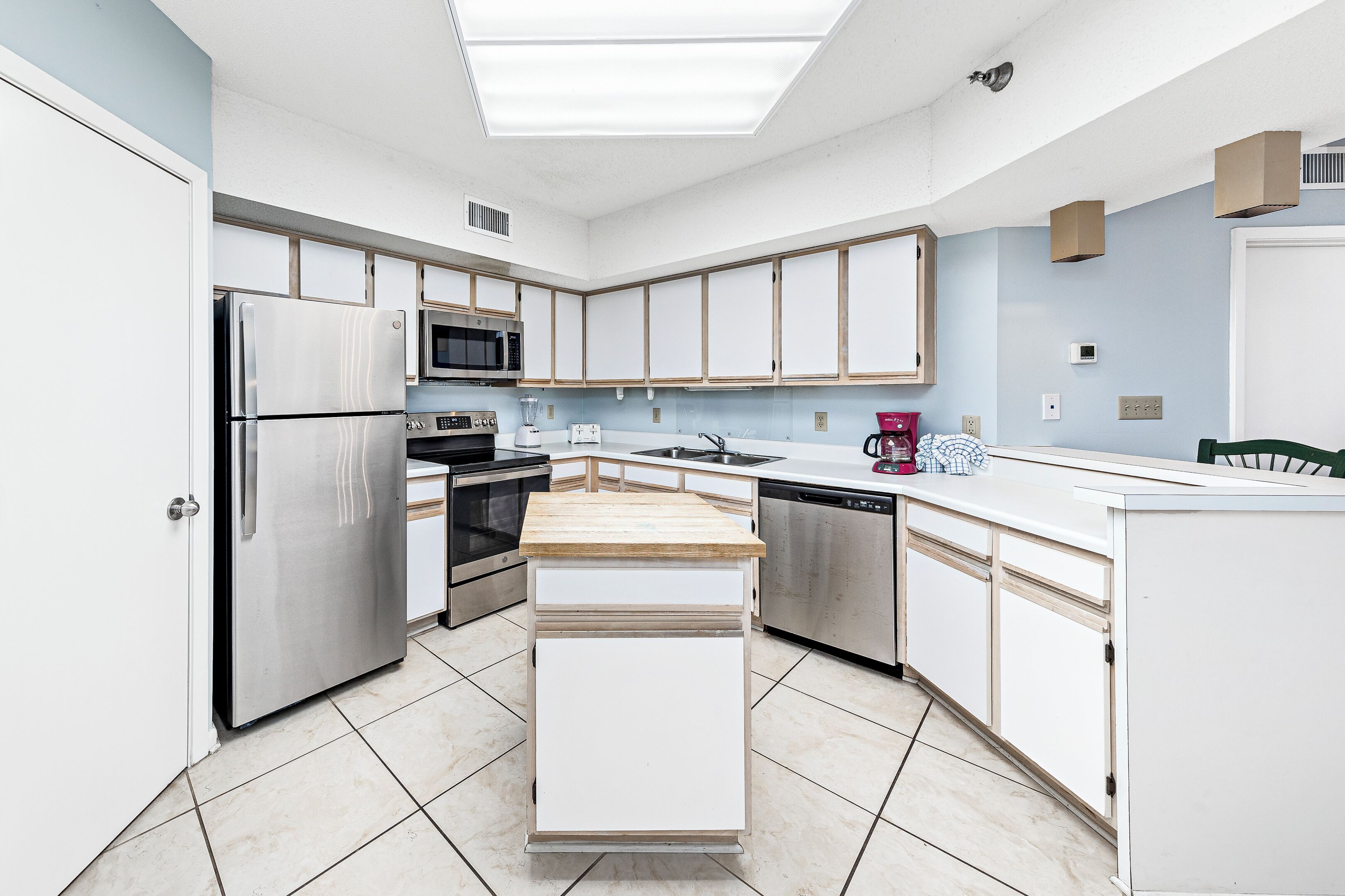 A modern kitchen with stainless steel appliances, white cabinetry, and a wooden countertop.