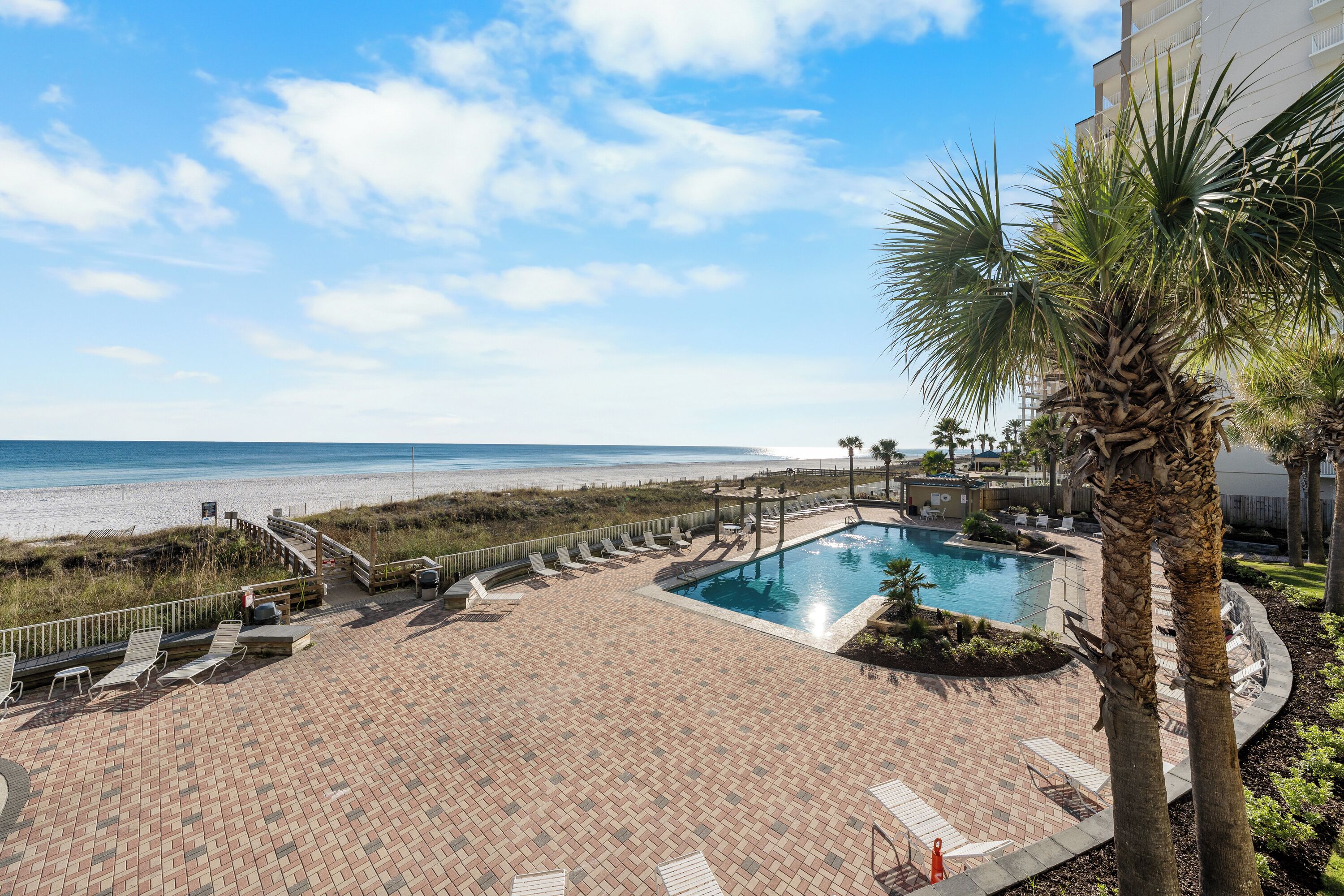 A pool area with lounge chairs and a view of the beach.