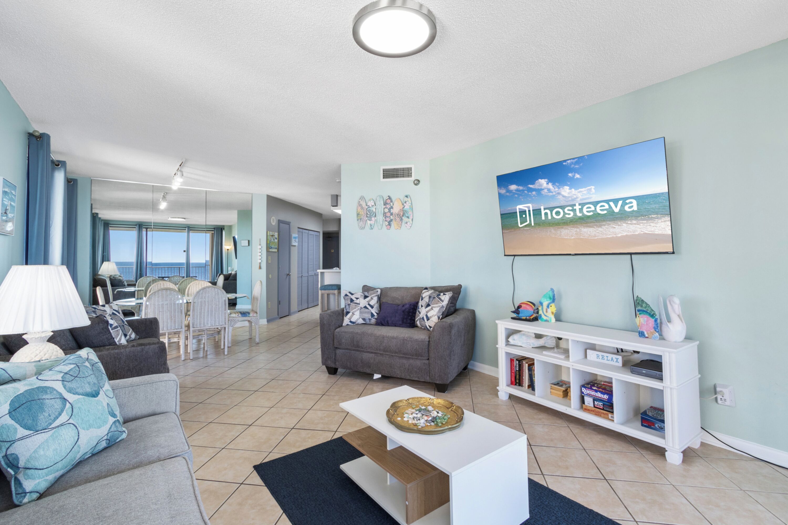 A living room with a grey sofa, a white coffee table, and a TV displaying 'Hosteva'.