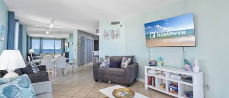A living room with a grey sofa, a white coffee table, and a TV displaying 'Hosteva'.