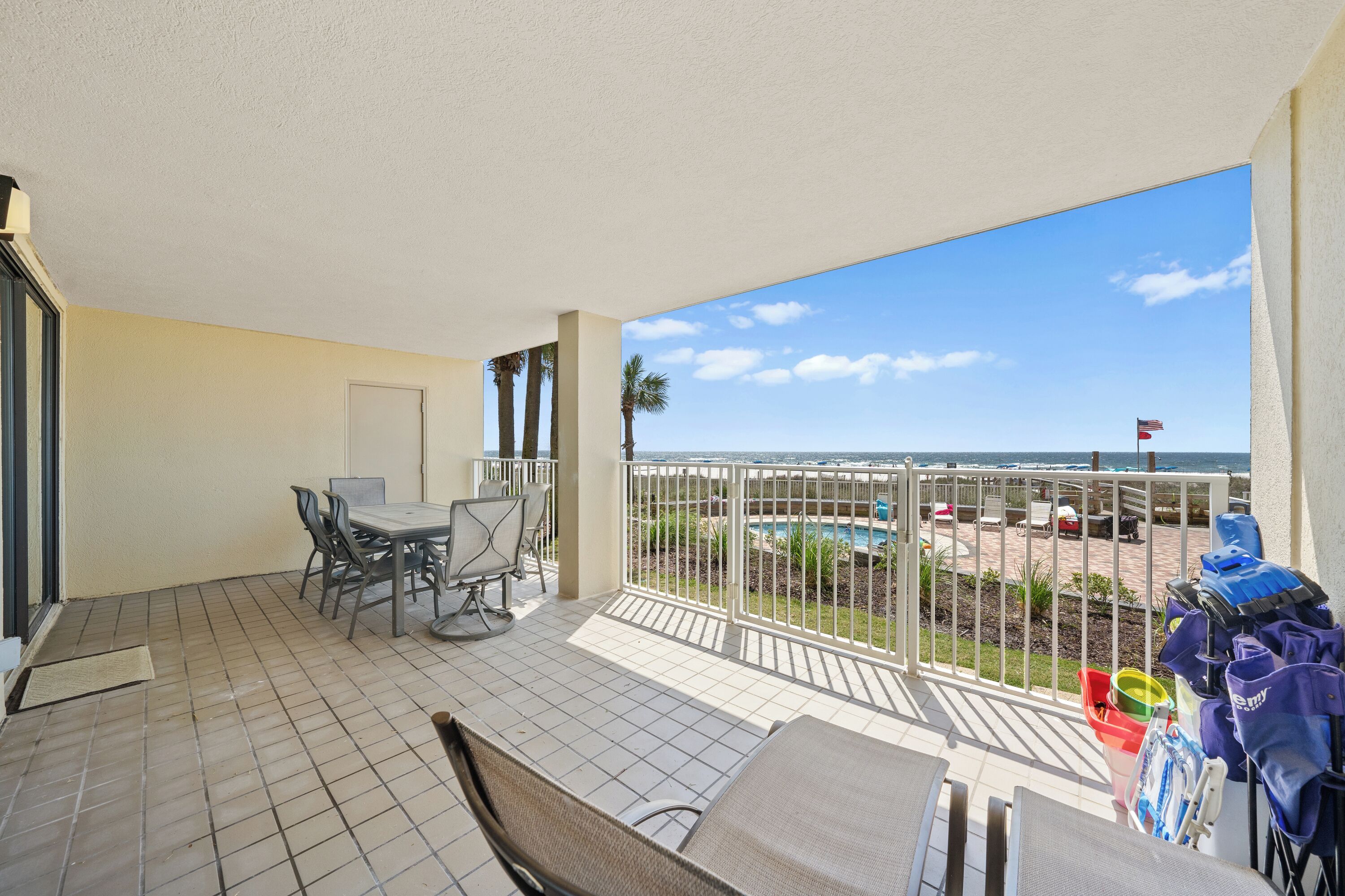 A balcony with a view of the beach, a table with chairs, and a railing with bags.