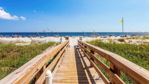 A wooden boardwalk leading to a beach with umbrellas and chairs. - White Caps Condos (Orange Beach)