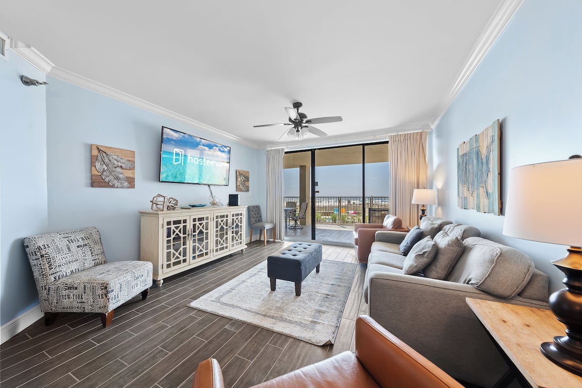 A modern living room with a flat-screen TV, a ceiling fan, and a view to the outside.