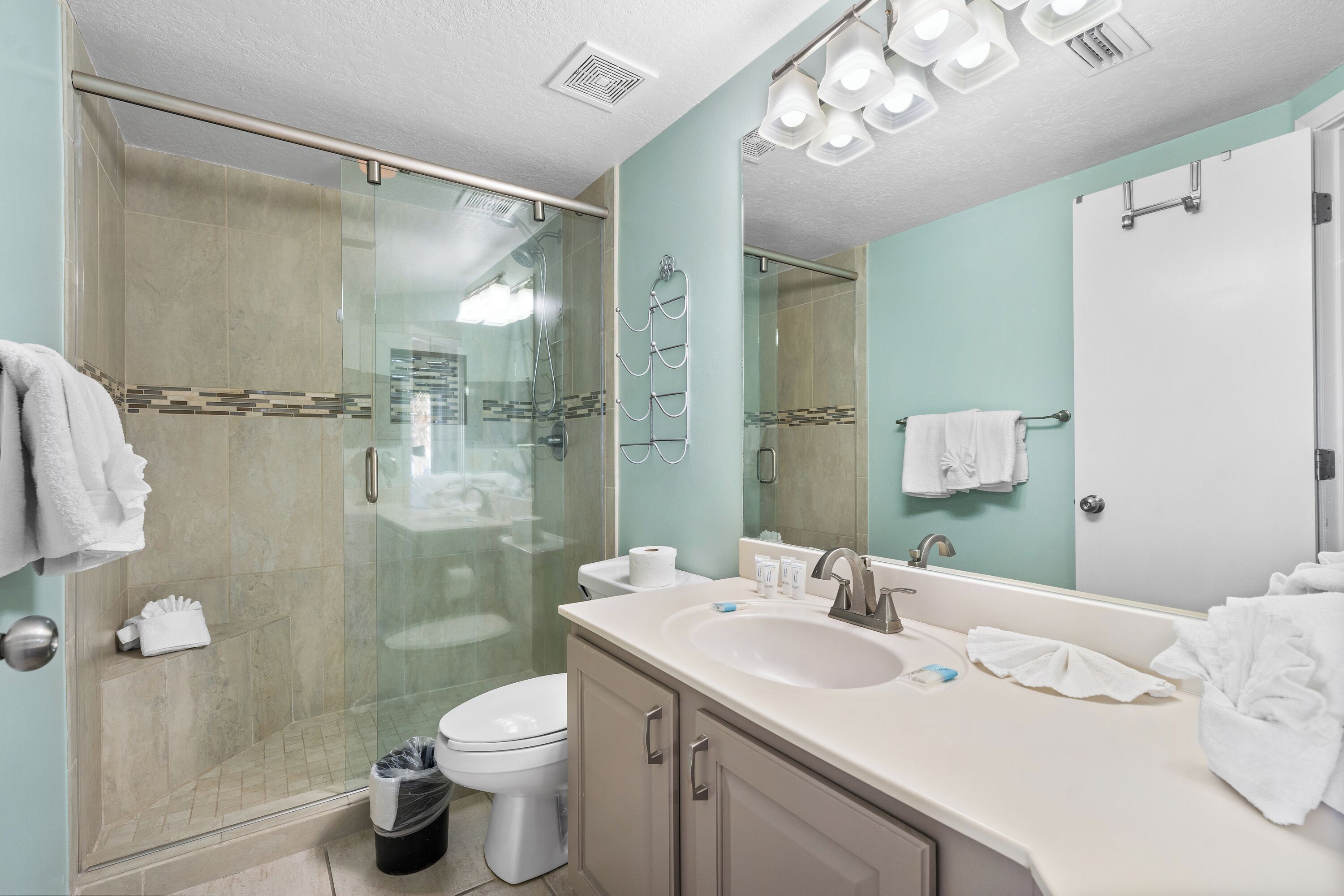 Un baño moderno con ducha envuelta en cristal, tocador doble y un espejo grande.