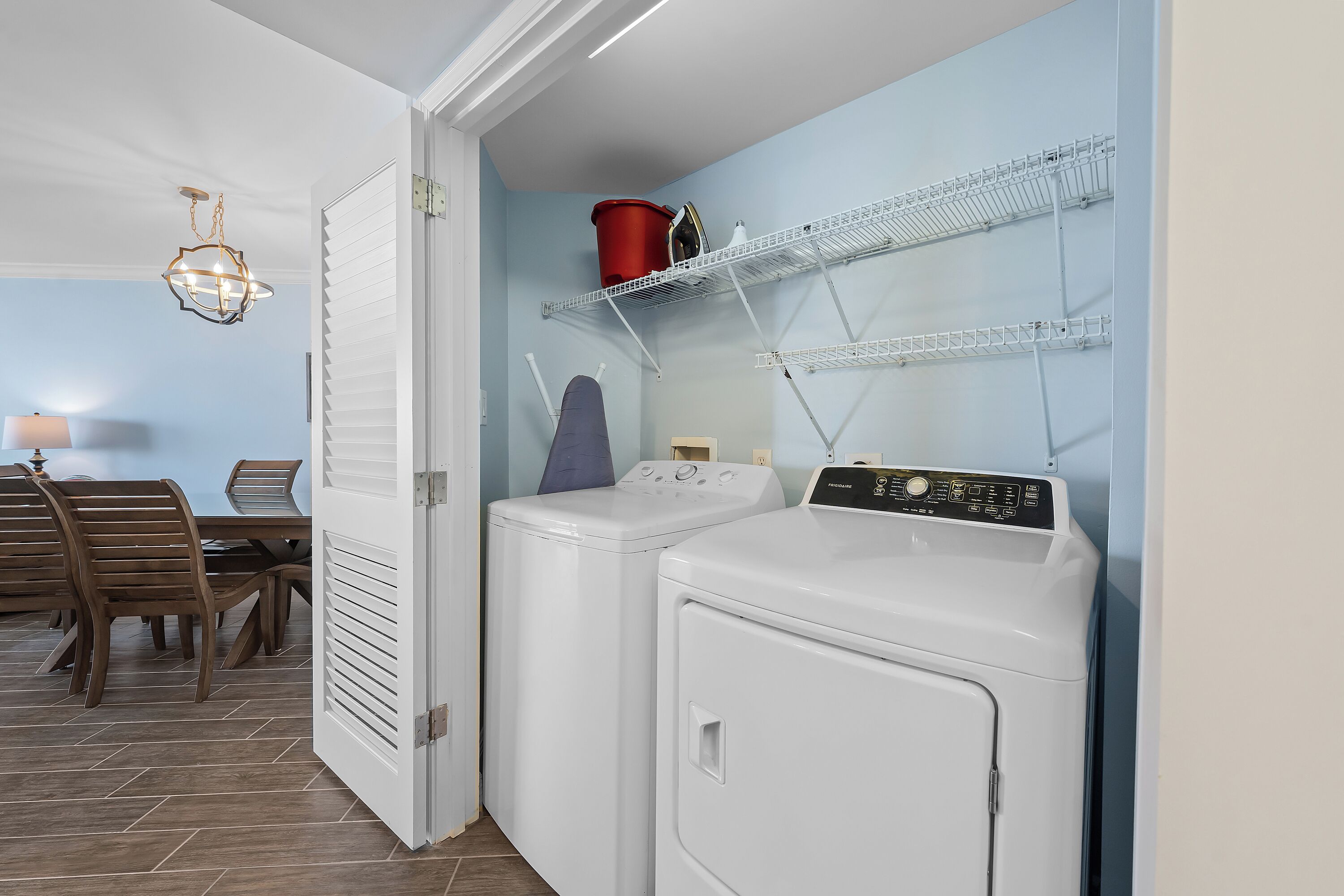 A laundry room with two white washing machines, a red bucket, and a drying rack on the wall.