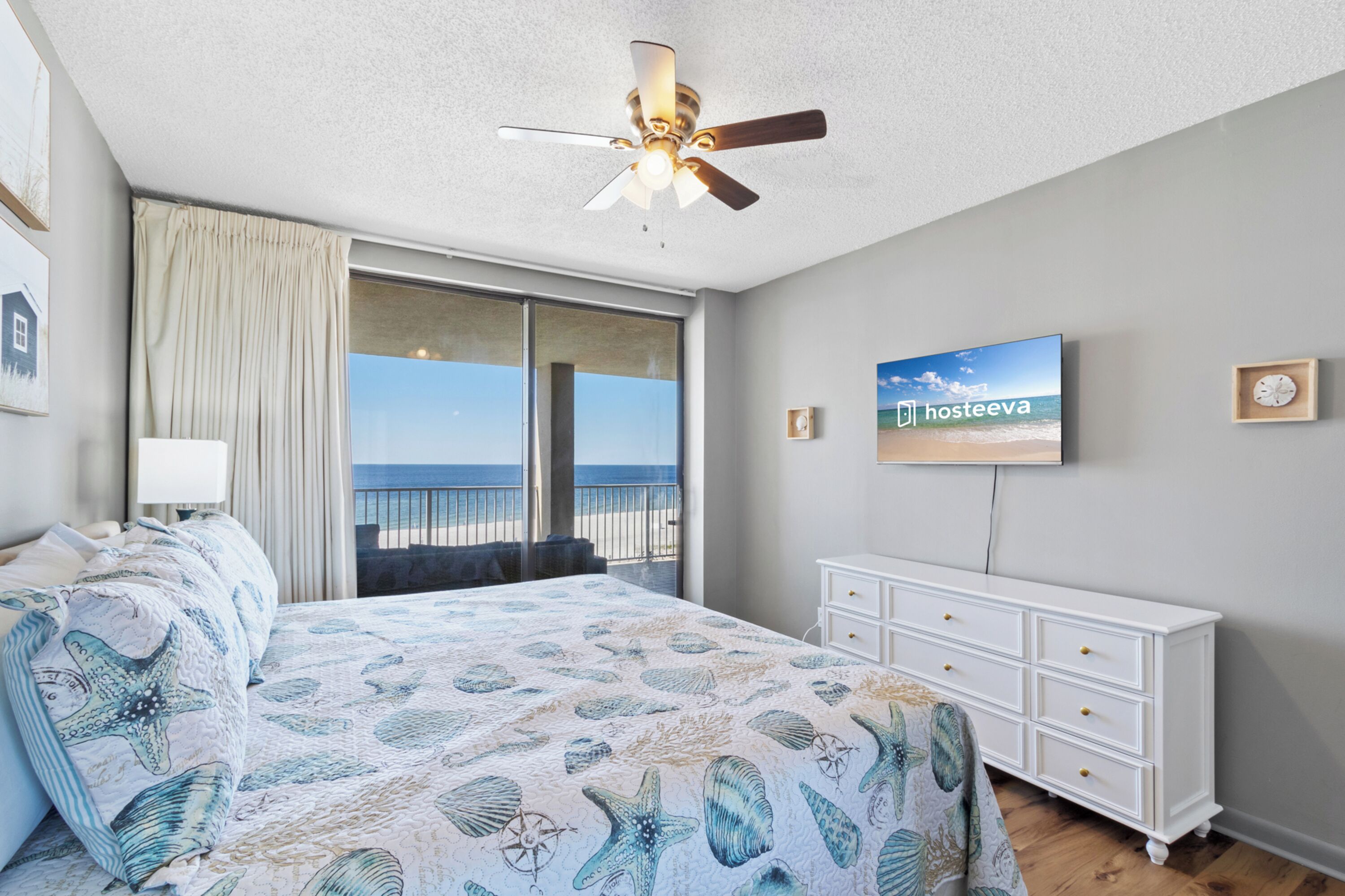 Un dormitorio con una cama grande, un ventilador de techo, un televisor y vistas a la playa.