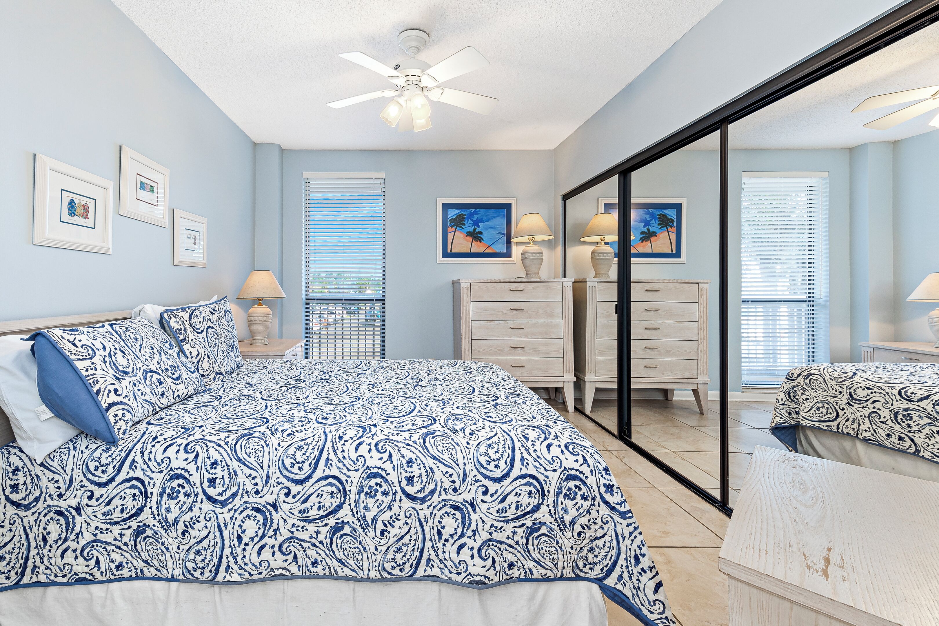 A bedroom with a bed, a dresser, a mirror, and a ceiling fan.