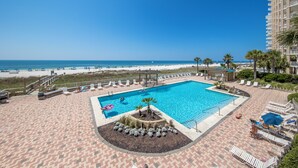 A rooftop pool with a view of the beach and ocean, surrounded by lounge chairs and palm trees. - White Caps Condos (Orange Beach)