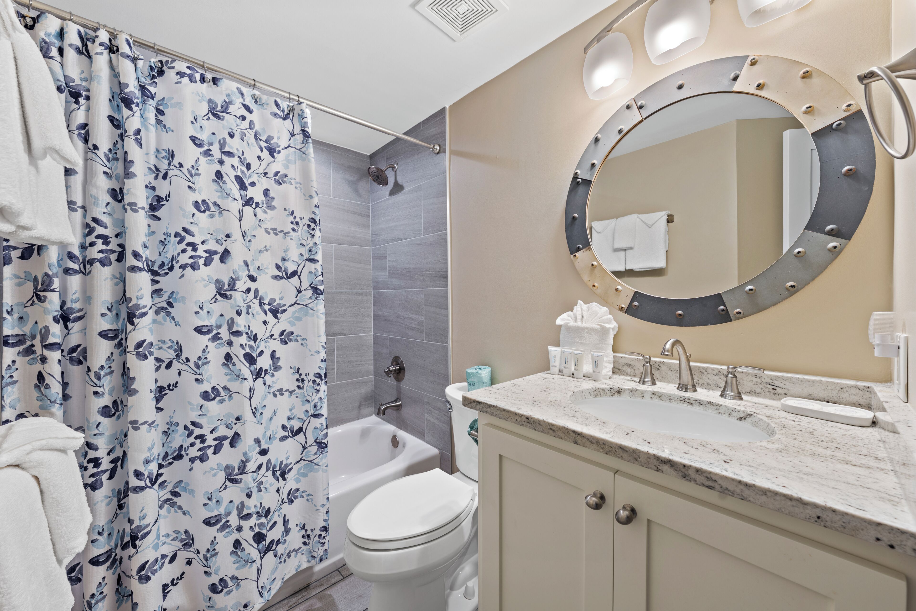 A bathroom with a shower curtain, a toilet, a sink, and a mirror.