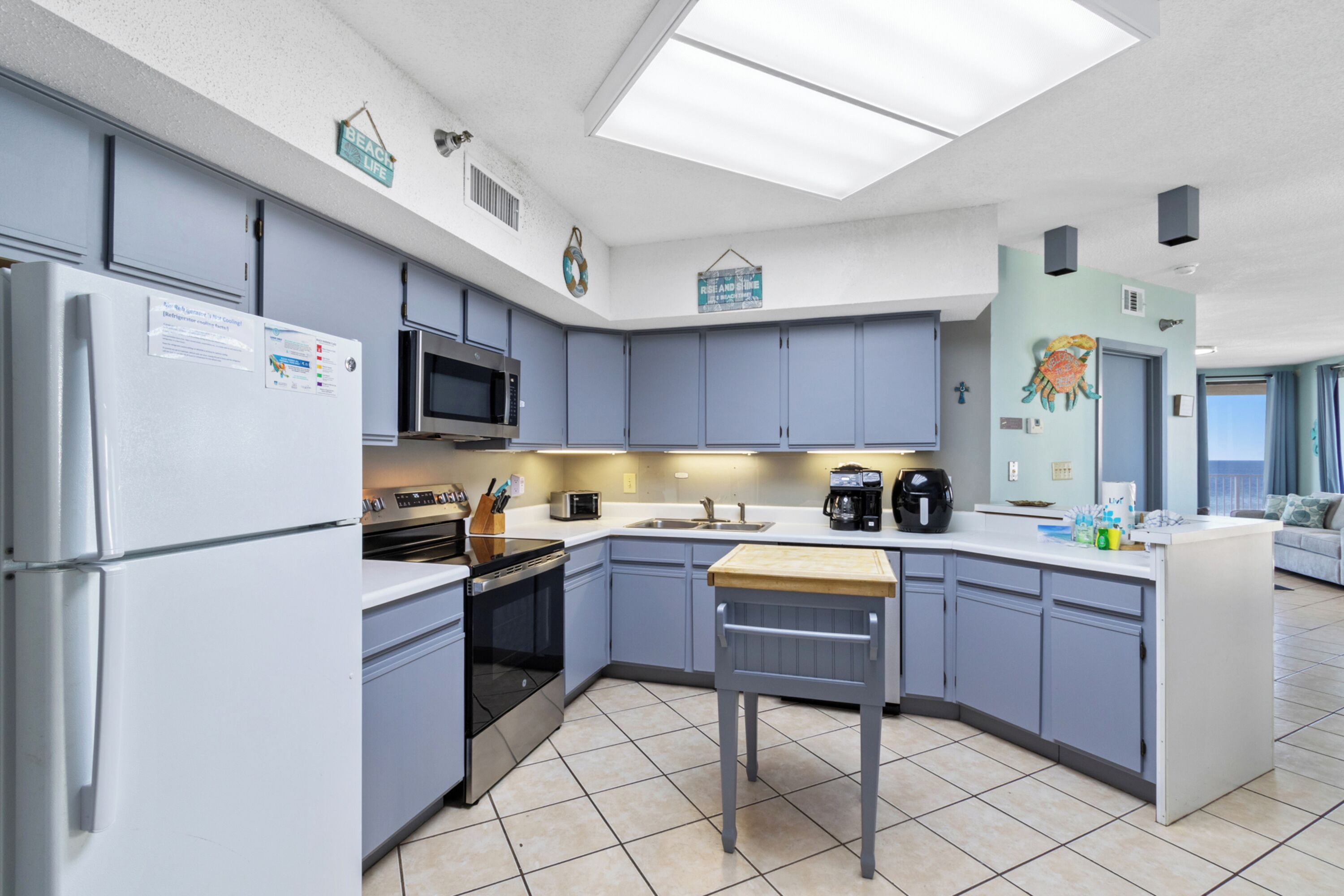 A modern kitchen with grey cabinets, a central island, a microwave, and a refrigerator.