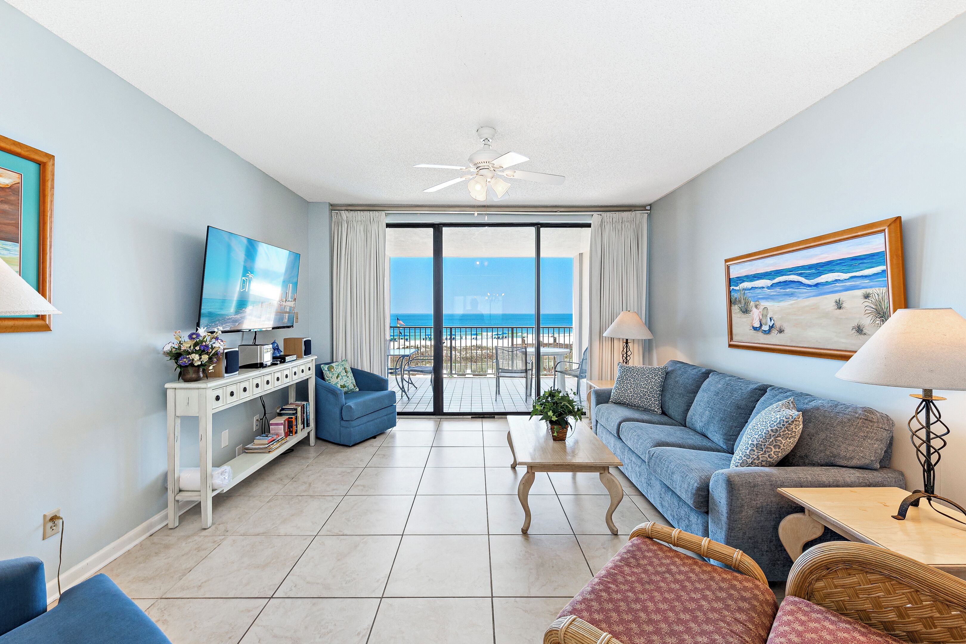 A living room with a television, a sofa, a coffee table, and a view of the ocean through large sliding glass doors.