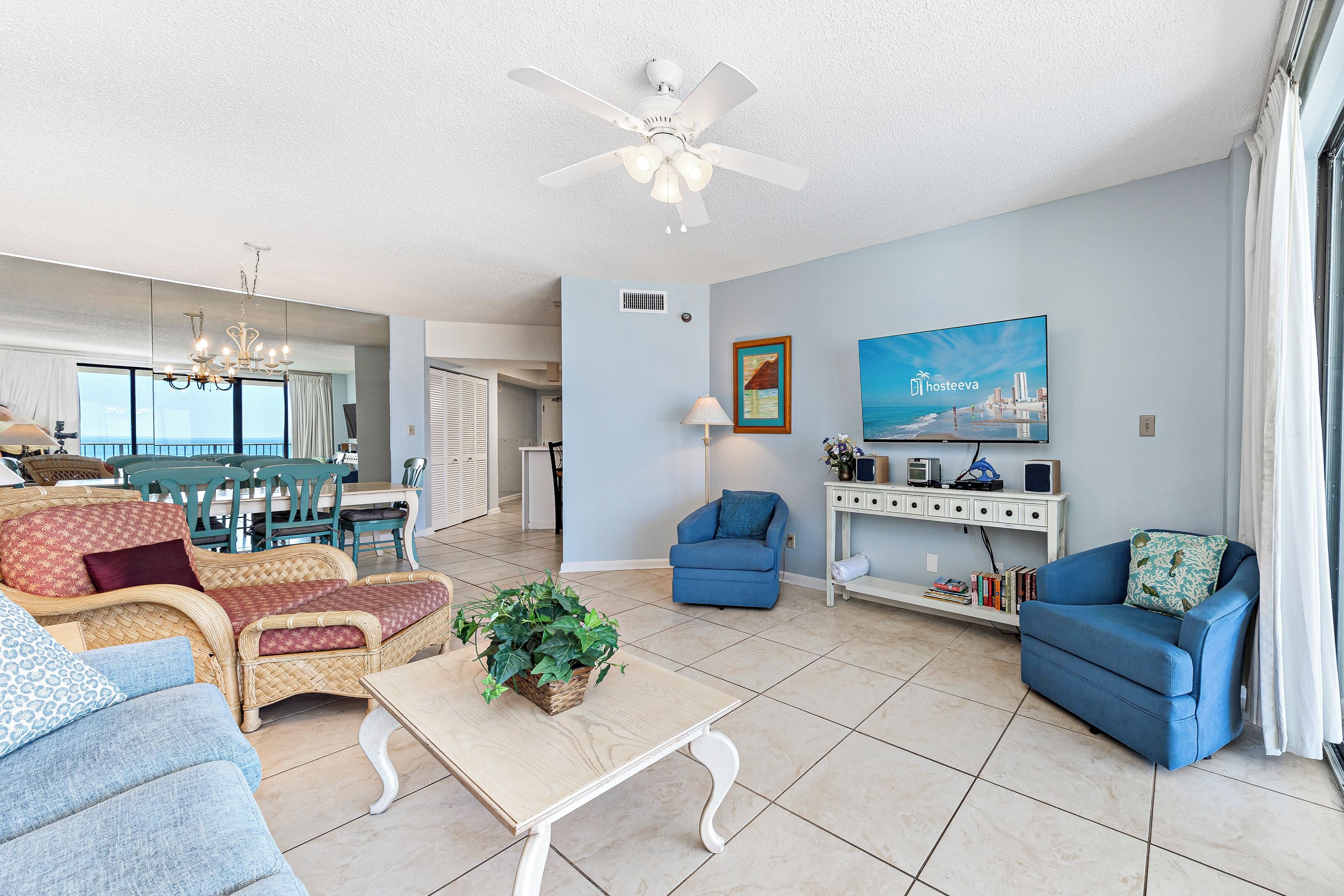 A spacious living room with a dining area, a ceiling fan, a TV, and a large window with curtains.