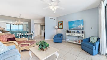 A spacious living room with a dining area, a ceiling fan, a TV, and a large window with curtains.
