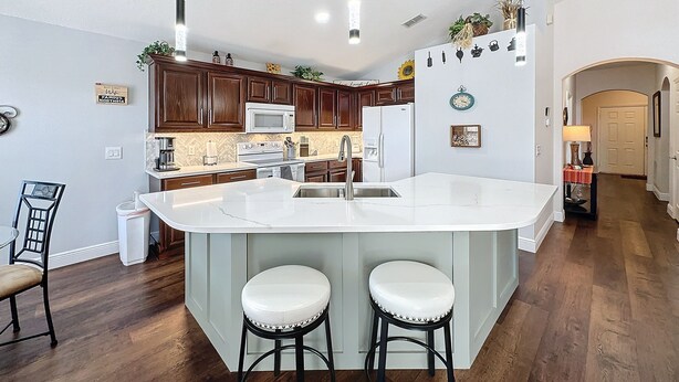 Une cuisine moderne dotée d’un grand îlot central, de meubles en bois foncé, d’appareils électroménagers blancs et de luminaires suspendus.