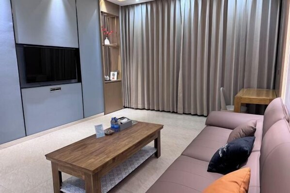 A modern living room with a wooden coffee table, a sofa, a TV mounted on a cabinet, and a large window with curtains. - Shangzhi Longmen Hotel (Shangzhi)