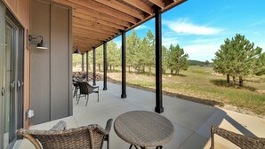 A covered patio with wicker furniture and a view of a forest. - Lazy Daze, Black Hills of SD (Sturgis)