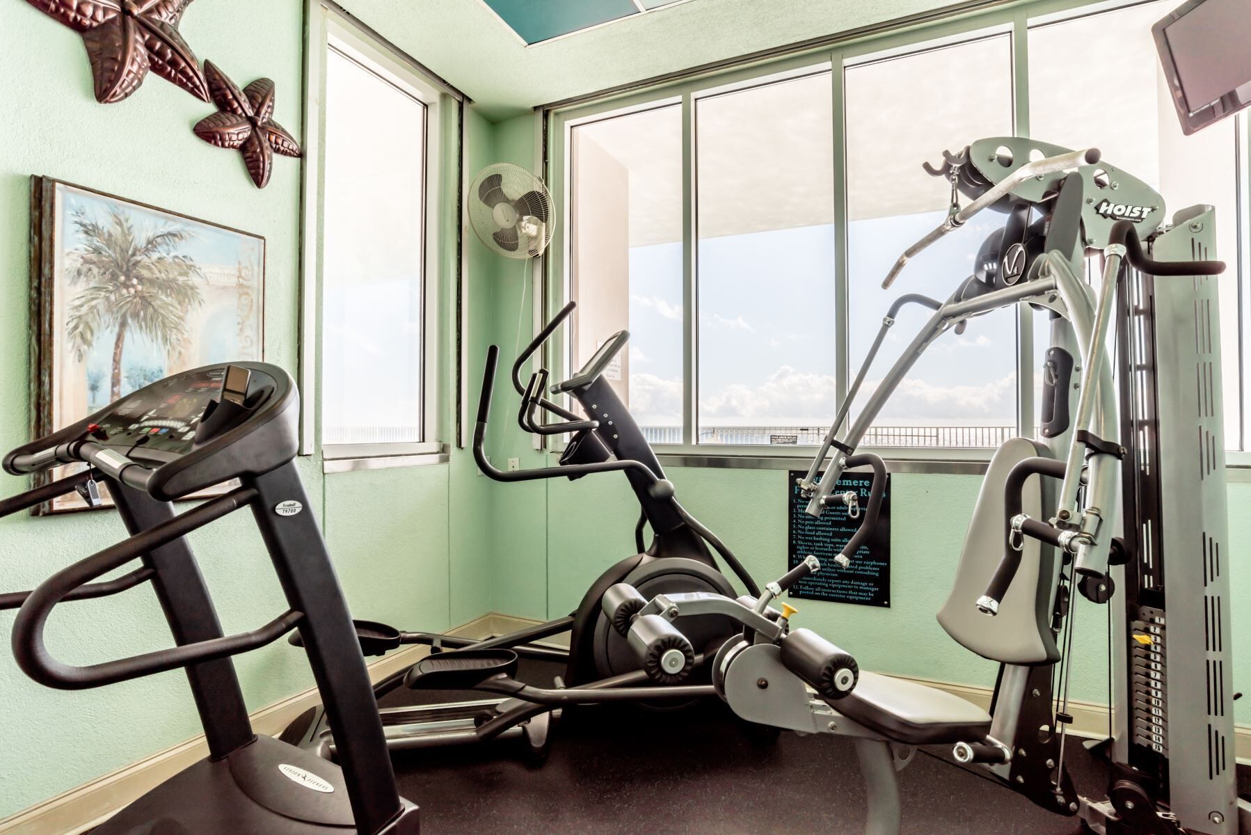A gym with exercise equipment, a treadmill, and a window with a view of the sky.
