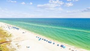 A beach with clear turquoise waters, a sandy shore, and a wooden walkway leading to the water.