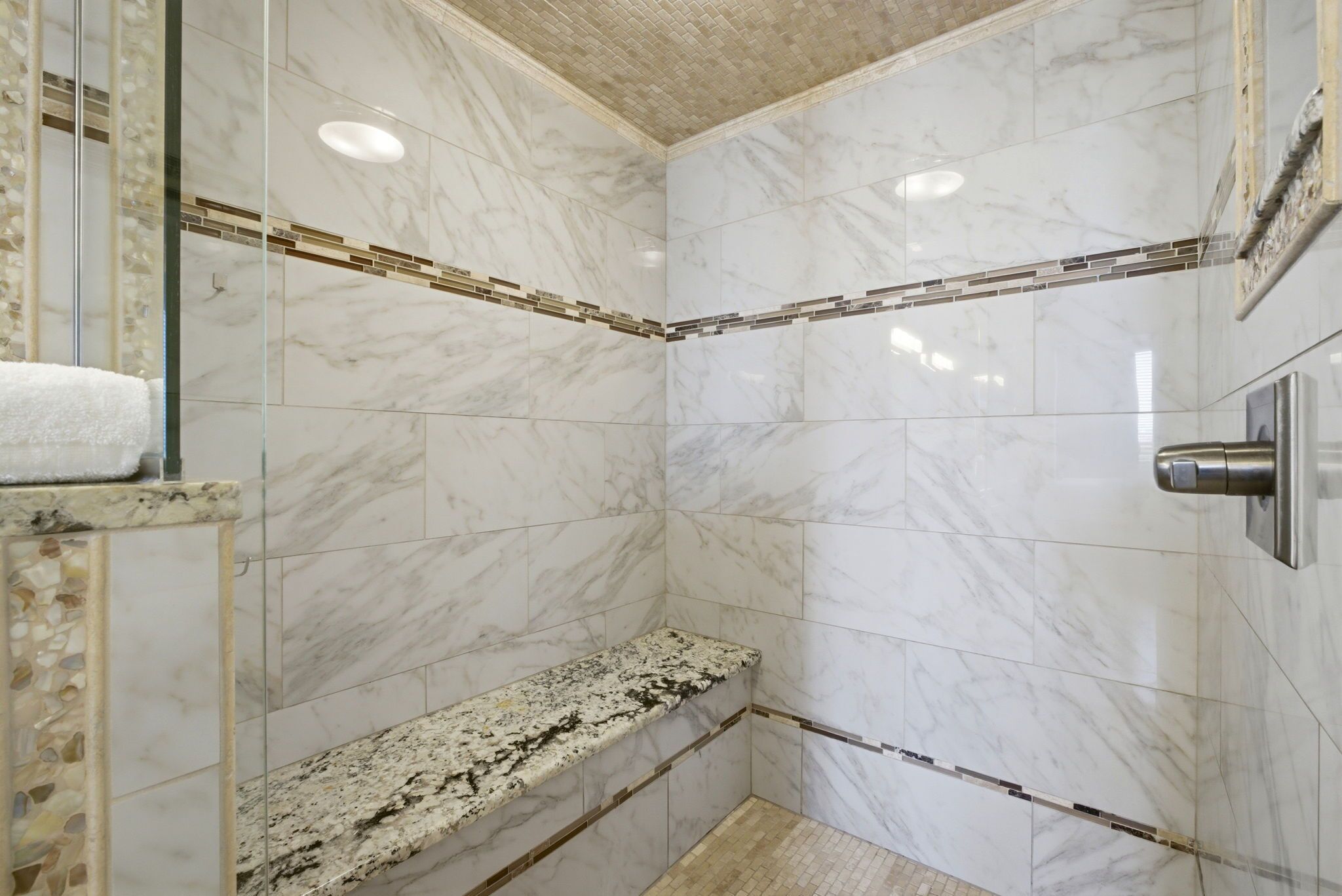 A corner shower with a bench, marble walls, and a tiled floor.