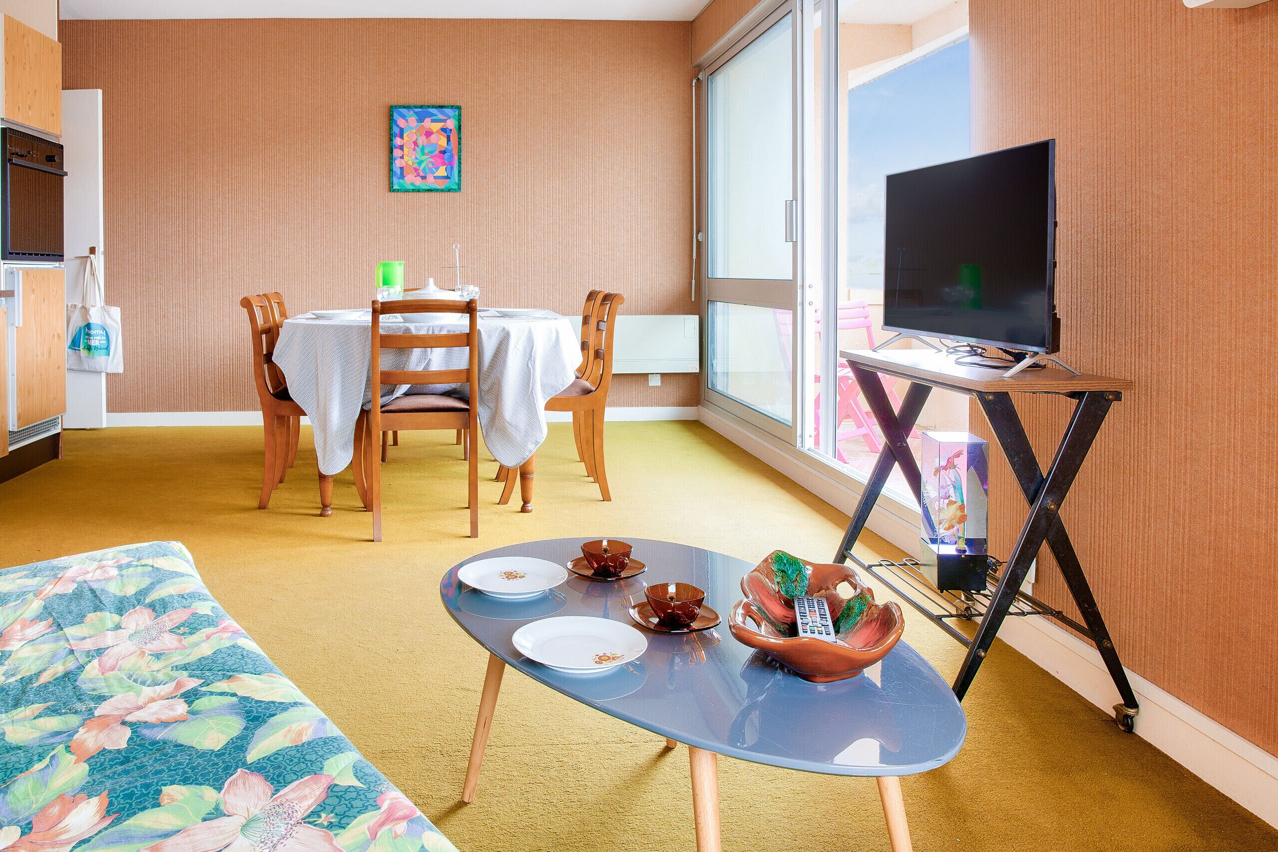 Ein kleines Hotelzimmer mit Essbereich, einem Fernseher auf einem Schrank und einem großen Fenster.