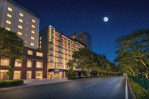 Un hotel con varios pisos, una entrada bien iluminada y un cielo despejado.