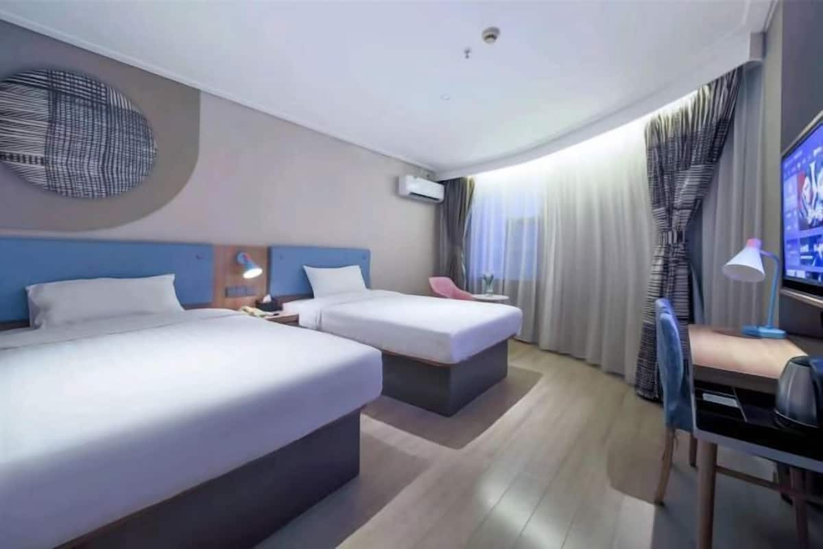 A hotel room with two beds, a desk, a chair, a TV, and a wall-mounted air conditioner.